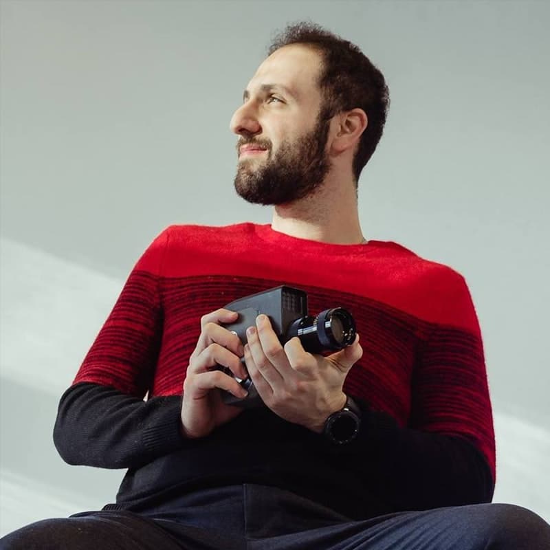 A filmmaker holding a vintage camera against a plain wall